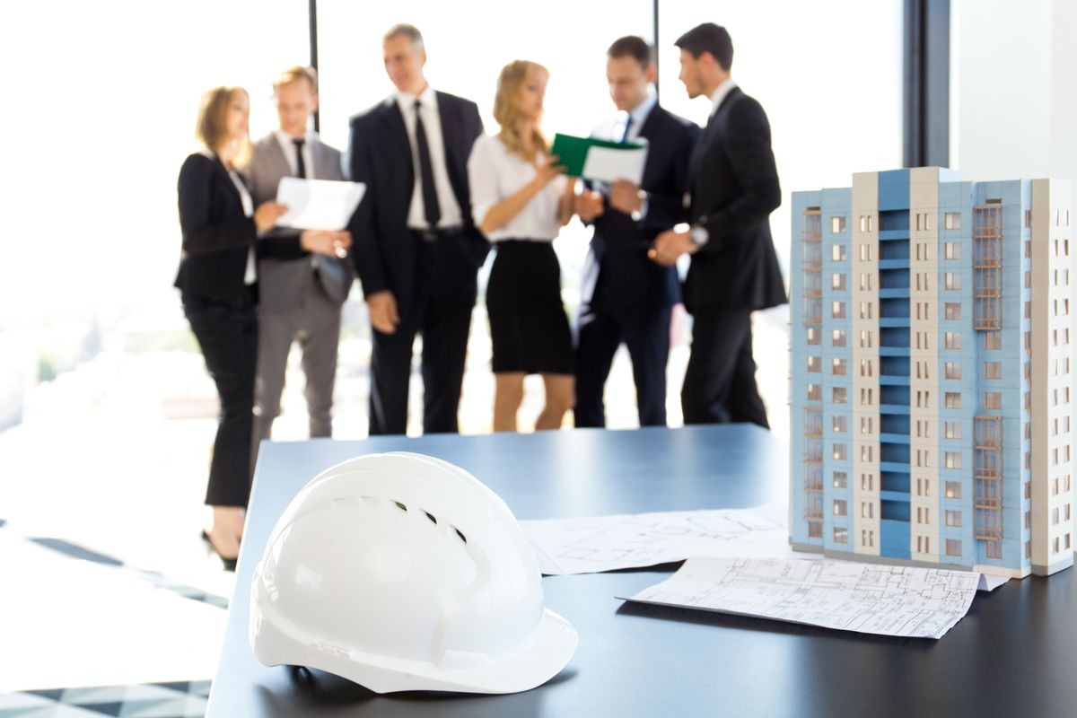 Business meeting of architects and investors, model of modern multi storey residential building house and hardhat on table , construction planning concept